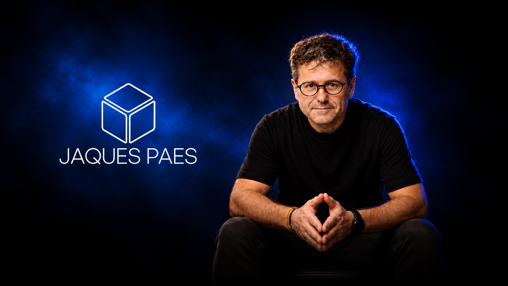Jaques Paes sentado, mãos juntas, sob luz azul, ao lado do logotipo Jaques Paes